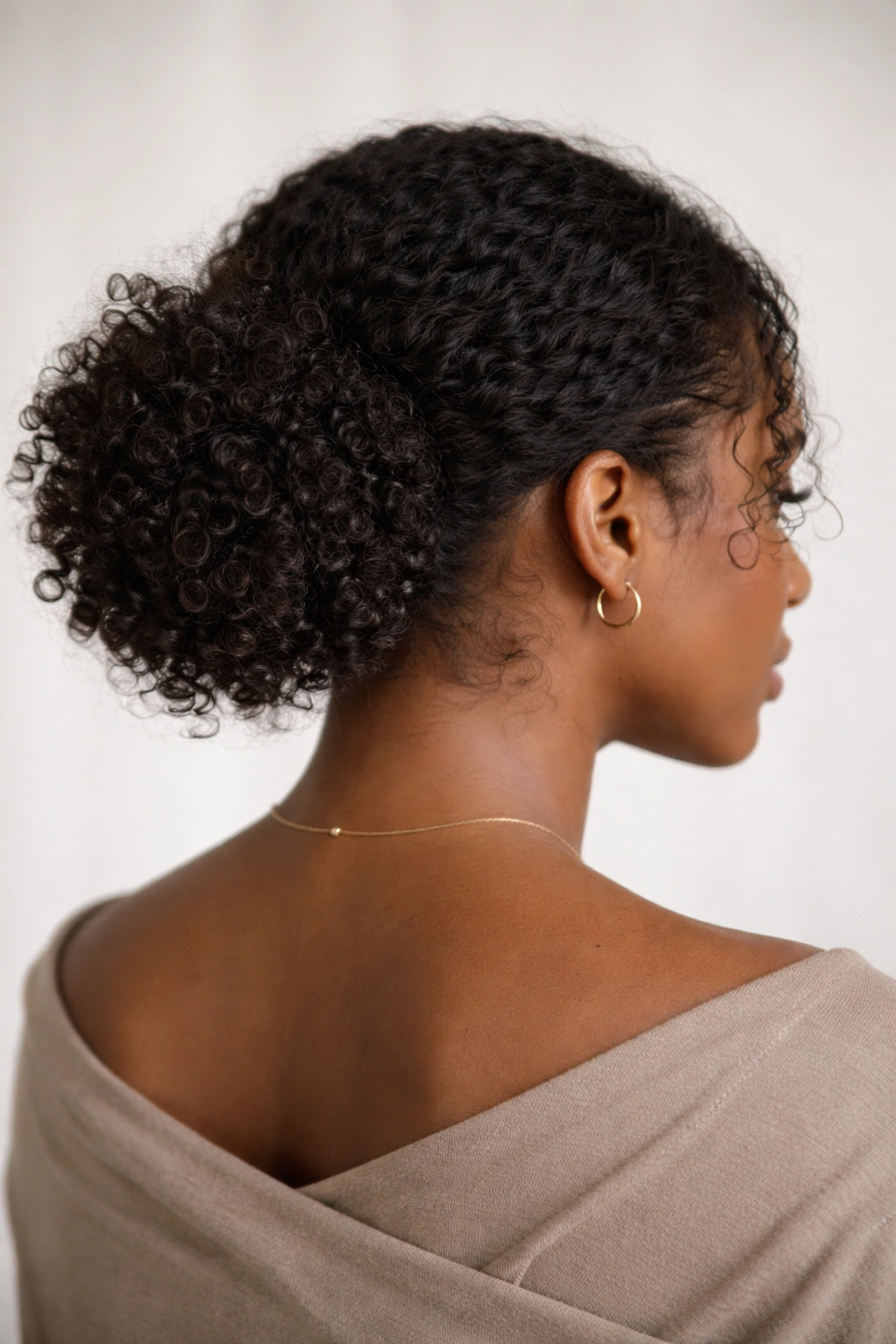 Curly hair gathered into a soft curly puff at the nape forming a low bun