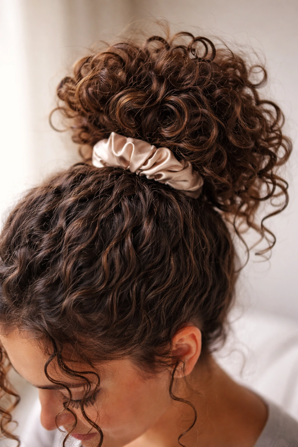Close-up of a high pineapple-style updo showing curly hair piled on top with a satin scrunchie