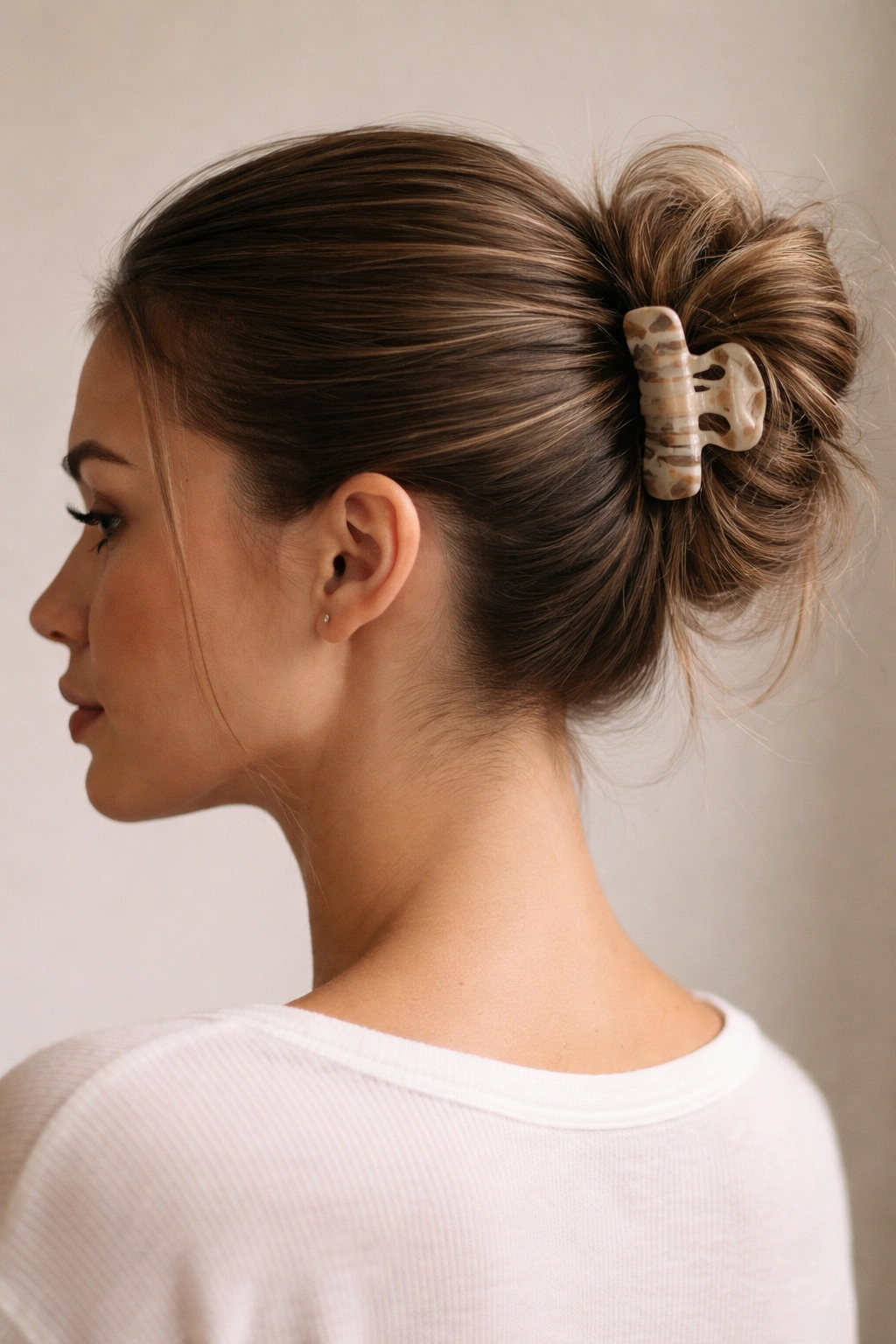 Close-up of a hairstyle with a sleek front and a textured messy bun secured by a claw clip