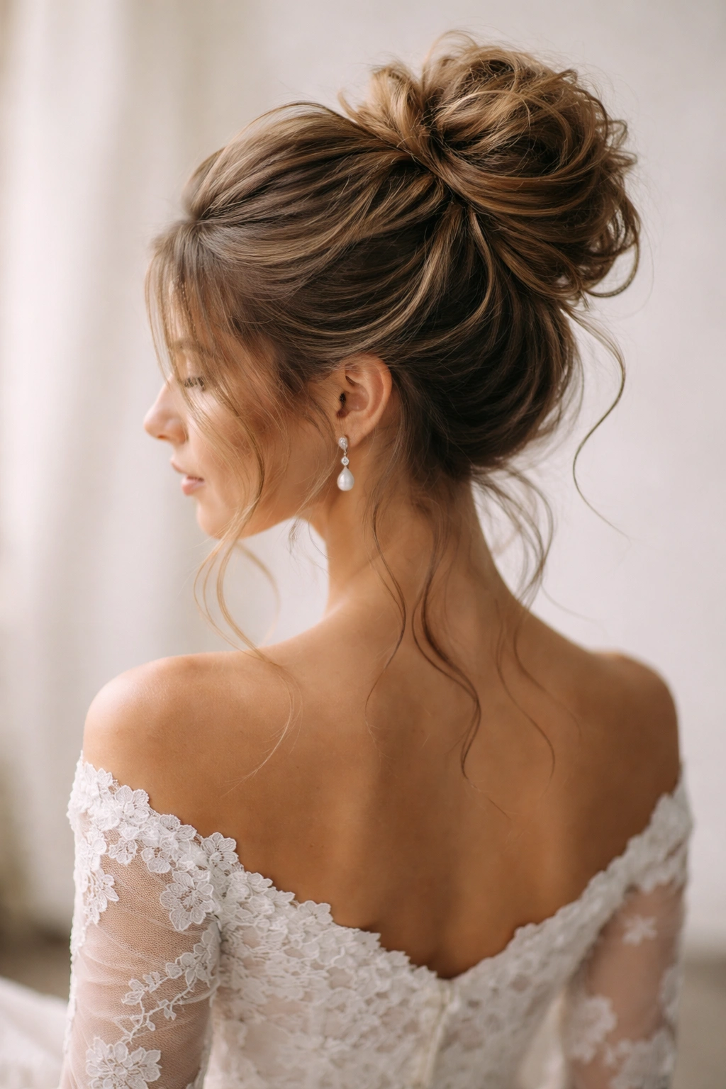Close-up of a high-volume teased bun with face-framing tendrils in bridal lighting