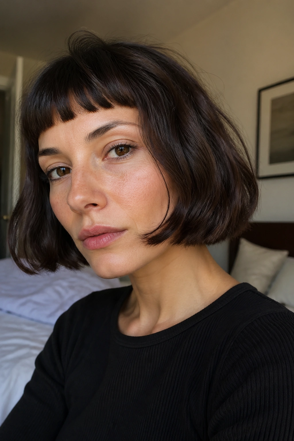 Close-up portrait of a woman with French bob and micro bangs in natural window light.